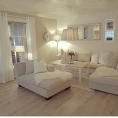 a living room filled with white furniture and lamps on top of wooden floored floors