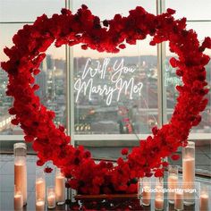 a heart - shaped arrangement with candles and flowers in front of a window that reads, will you marry me?