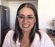 a woman wearing glasses and smiling in front of a refrigerator with an icebox behind her