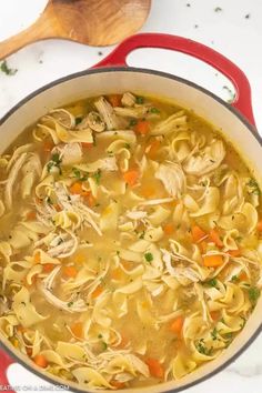 a red pot filled with chicken noodle soup and a wooden spoon in the bowl