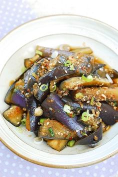 a white plate topped with eggplant covered in sesame seeds and garnish