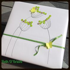 a present wrapped in white paper with green ribbon and flowers drawn on the wrapping paper