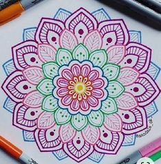 a coloring book with markers and pens on the table next to it is an image of a colorful flower