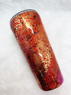 a red and gold glitter tumbler sitting on white fur