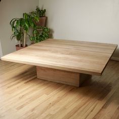 a wooden table sitting on top of a hard wood floor next to a potted plant