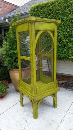 a green birdcage sitting on top of a cement floor next to a bush