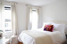 a bed with white sheets and pillows in a bedroom next to two window sills