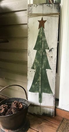 a wooden sign with a christmas tree on it next to a potted pine cone