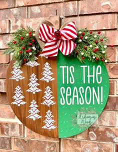 a wooden sign that says tis the season and decorated with evergreens, pine cones and red berries