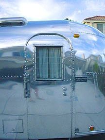 a shiny silver trailer parked in front of a house on the side of a road