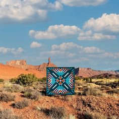 a blue quilt sitting on top of a dirt field next to mountains and clouds in the sky