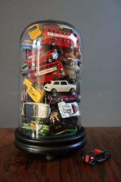 a glass dome with cars and trucks inside on a wooden table next to a toy car