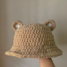 a crocheted bear hat with ears is held up in the air by someone's hand