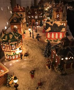 a christmas village is shown with lights and snow on the ground in front of it