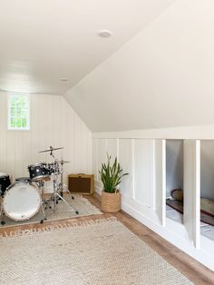 there is a drum set in the corner of this room with white walls and wood flooring