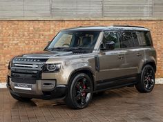 a grey land rover is parked in front of a brick wall with black rims