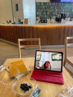 a tablet sitting on top of a wooden table next to a bowl of fruit and an open book