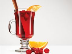 a glass mug filled with red liquid and garnished with cherries next to an orange slice