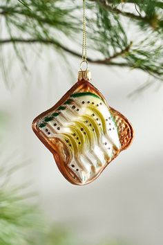 a glass ornament hanging from a tree branch with green and yellow designs on it