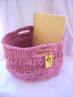 a pink crocheted basket with a notepad in the bottom and a yellow tag attached to it