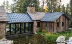 a house that is made out of wood and stone, with a metal roof in the woods