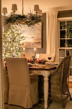 a dining room with a christmas tree in the corner and candles lit on the table