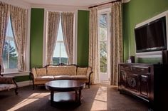 a living room with green walls and curtains on the window sill, two couches, a coffee table, and a flat screen tv