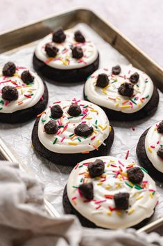 chocolate cookies with white frosting and sprinkles are on a baking sheet