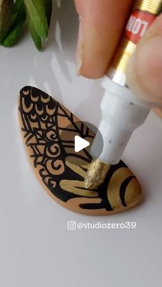 someone is using a sharp tip to paint a wooden shoe with gold and black designs on it