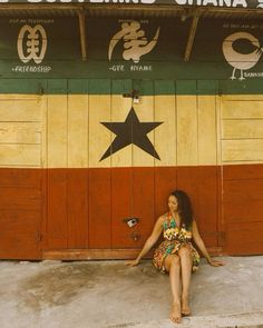 a woman sitting on the ground in front of a building with stars painted on it