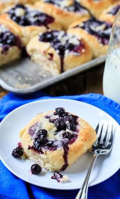 a blueberry muffin on a white plate with a fork and glass of milk