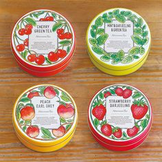 three round tins with labels on them sitting on a wooden surface, each containing strawberries and cherries