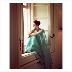 a woman in a green dress sitting on a window sill