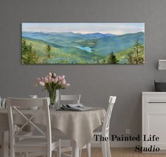 a painting on the wall above a dining room table with chairs and flowers in vase