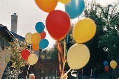 a bunch of balloons are floating in the air near a house and lawn with trees