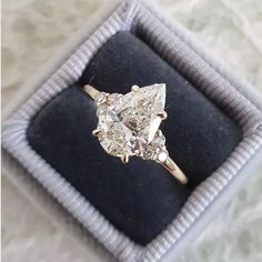 an engagement ring with two pear shaped diamonds on it in a velvet box, sitting on top of a cloth covered surface