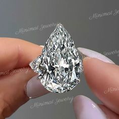 a close up of a person's hand holding a fancy ring with a pear shaped diamond