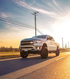 a white ram truck driving down the road with power lines in the background at sunset