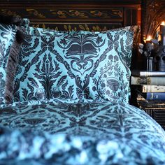 a bed covered in blue and brown pillows next to a stack of books on a table