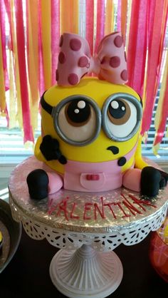 a cake that looks like a minion on top of a table with pink and yellow streamers