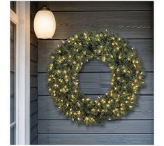 a christmas wreath hanging on the side of a house next to a light bulb and door