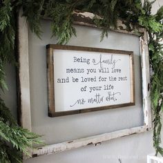 a sign hanging on the side of a wall with greenery around it that says being a family means you will love and be loved for the rest of your life