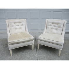 two white chairs sitting next to each other in front of a garage door on concrete