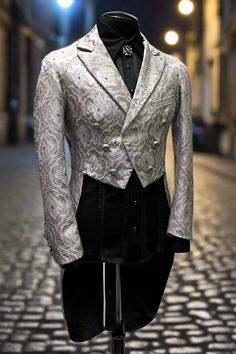 An grand gentleman's tailcoat from the days of Napoleon. A formal jacket with tails made in rich silver brocade. The jacket is cut short in front with extra long pleated tails in back. Decorated on the front with six vintage style metal lion buttons with smaller matching buttons at each cuff. This jacket is lined in sleek black satin with one left side breast pocket on the outside and one inside pocket on the right side. Comes in sizes Small-3X. So fine! Measurements: Small - Chest 40" Waist 30- Fitted Luxury Brocade Outerwear, Formal Fitted Brocade Outerwear, Fitted Brocade Formal Outerwear, Luxury Fitted Brocade Outerwear, Elegant Fitted Outerwear For Costumes, Elegant Long Sleeve Costume Suit, Fitted Silver Blazer For Evening, Elegant Brocade Tuxedo For Wedding, Semi-formal Fitted Brocade Blazer