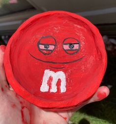 a hand holding up a painted red frisbee with the letter m on it