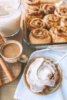 cinnamon rolls with icing on a plate next to a cup of coffee and spoon