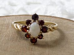 FREE DELIVERY - Reduced Australia/Canada * Full hallmark * Opal and Garnet * Good vintage condition This opal and garnet stone ring is very pretty. The garnets are surrounding a very attractive opal. The 9ct gold band has full hallmarks and is in good condition. A pretty dress ring, it would make a lovely gift for someone special. I'm sure you're someone special aren't you?? Approx size: Face 1/2 in height, 7/16 in width, Band - 2mm Ring size -  M - UK, 6.25 - US Approx weight: 1.8 gms VP002430- Garnet Opal Engagement Ring, Opal And Garnet Ring, Oval Garnet Cluster Ring In Gold, Oval Multi-stone Garnet Rings, Garnet Gold Ring, Victorian Multi-stone Opal Ring As Gift, Garnet Stone Ring, Garnet And Gold, Ring Opal