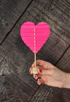 a person holding a pink heart shaped lollipop on a stick with the word i love you written on it