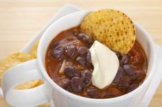 a white bowl filled with chili and beans next to a tortilla chip on top of a wooden table