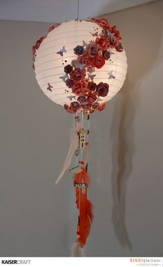 a paper lantern with flowers and feathers hanging from it's side on the wall